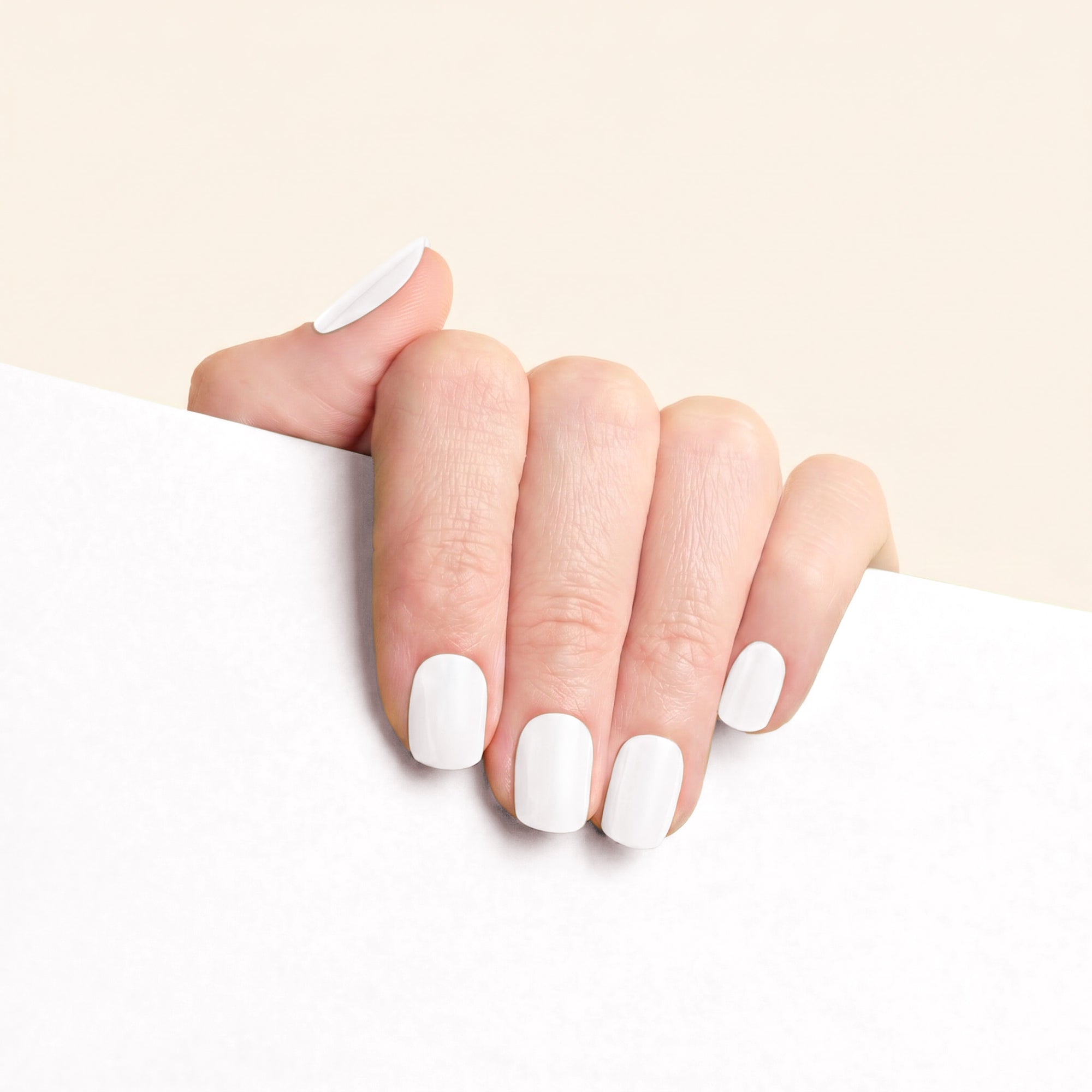 Short glossy white mesme nail wraps on hand with soft neutral background.