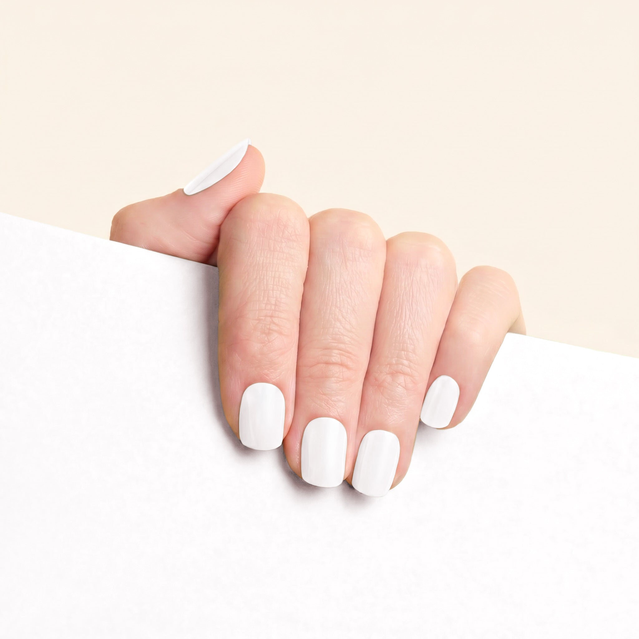 Short glossy white mesme nail wraps on hand with soft neutral background.