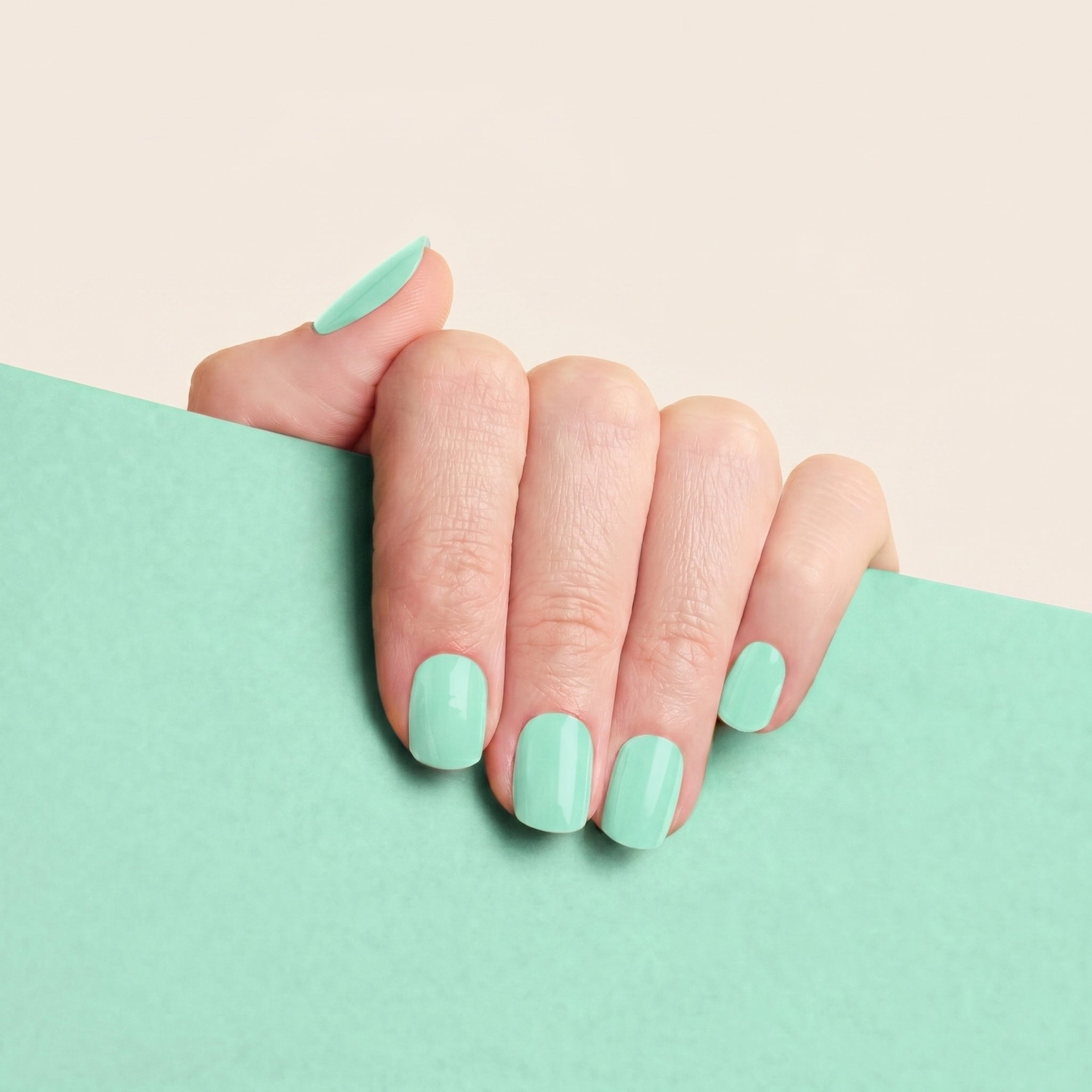 Glossy mint green mesme nail wraps on hand with soft mint background.