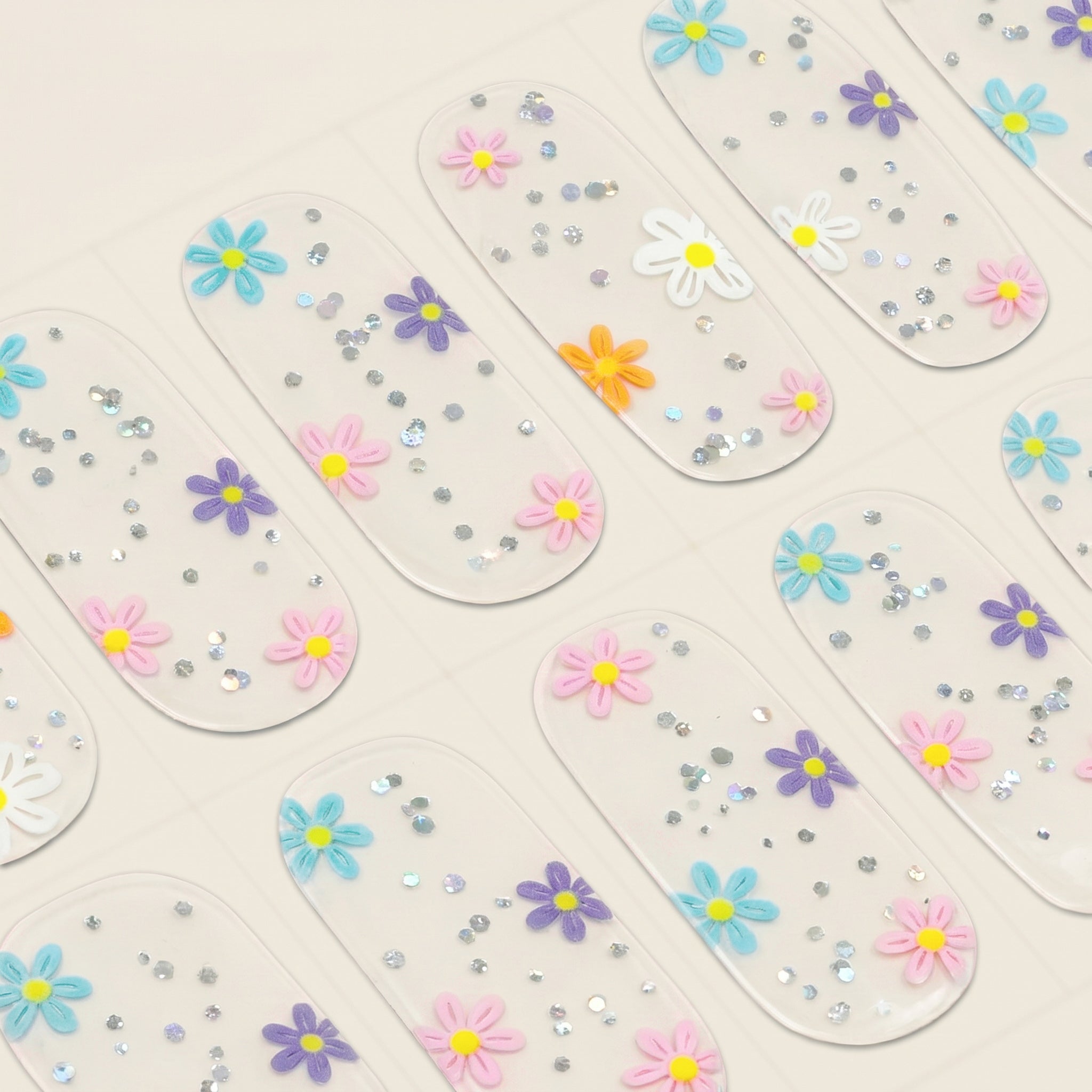 Close-up of clear mesme gel nail wraps with colourful daisy flowers and silver sparkle details.