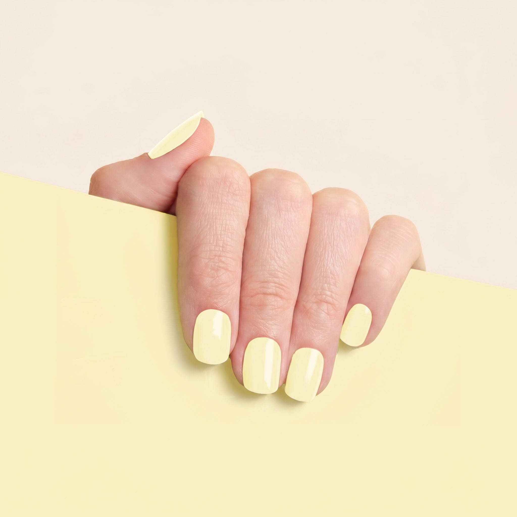 Hand with light yellow nail wraps on a matching background