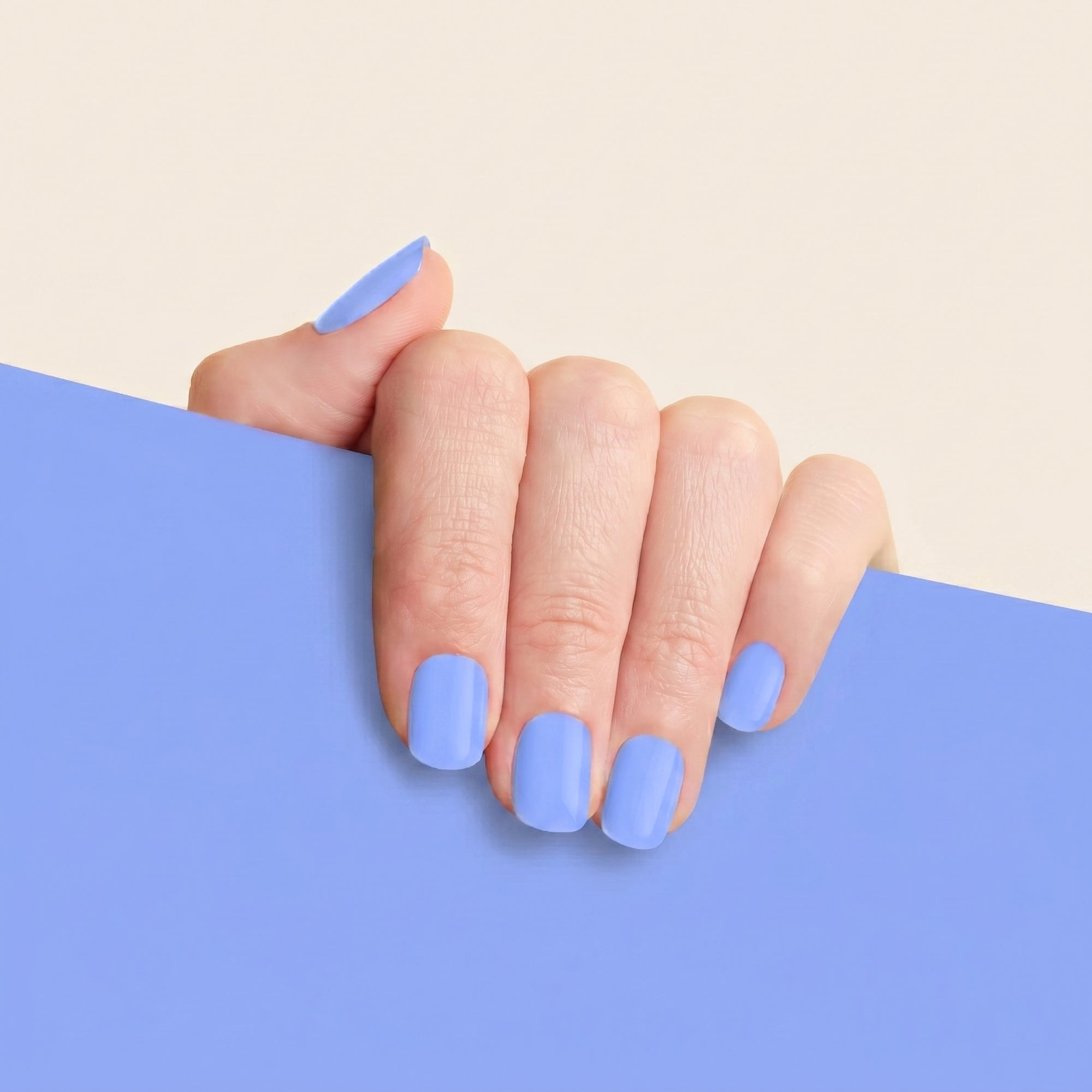 Hand with glossy periwinkle blue mesme STAY gel nail wraps against a matching blue background.