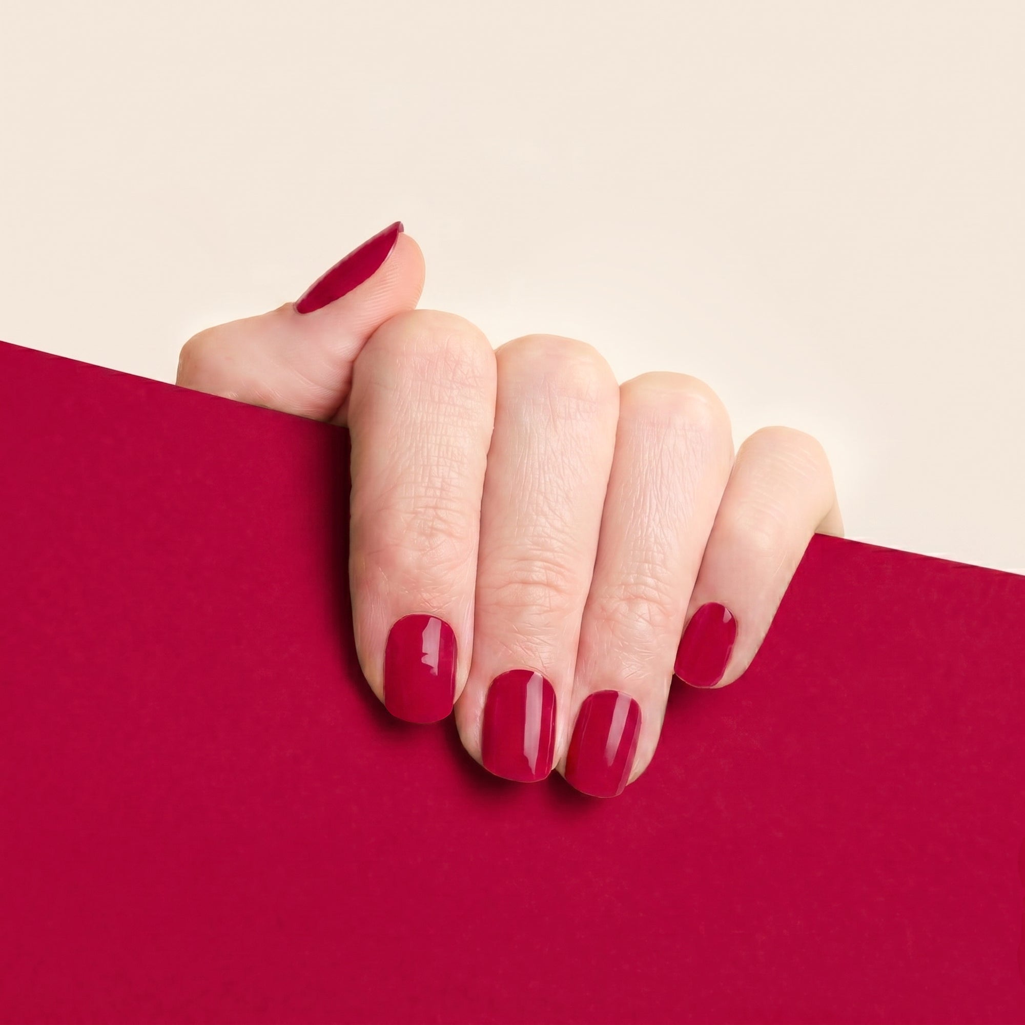 Hand with glossy deep red mesme gel nail wraps against a matching red background.