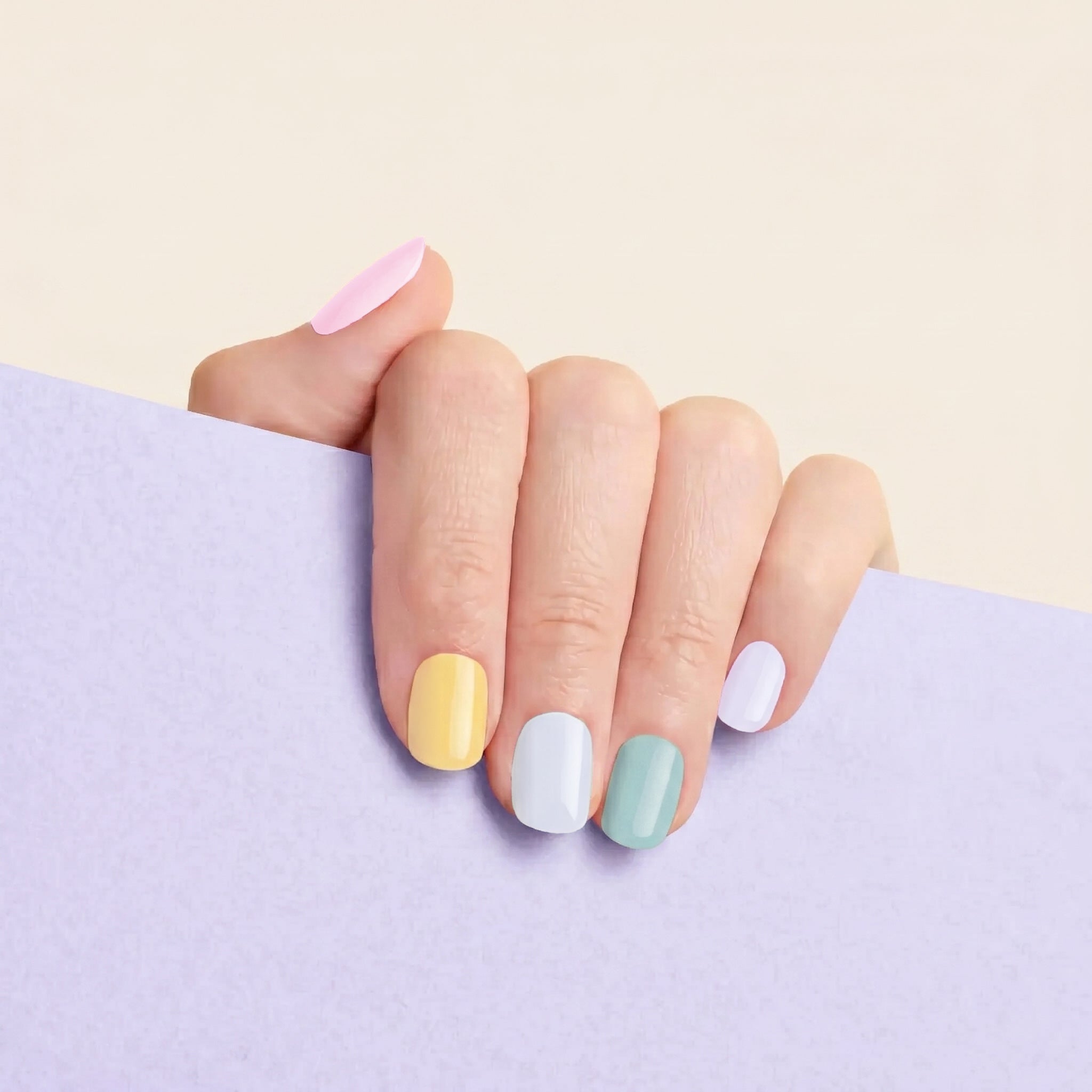 Hand with mesme pastel nail wraps on a light purple background