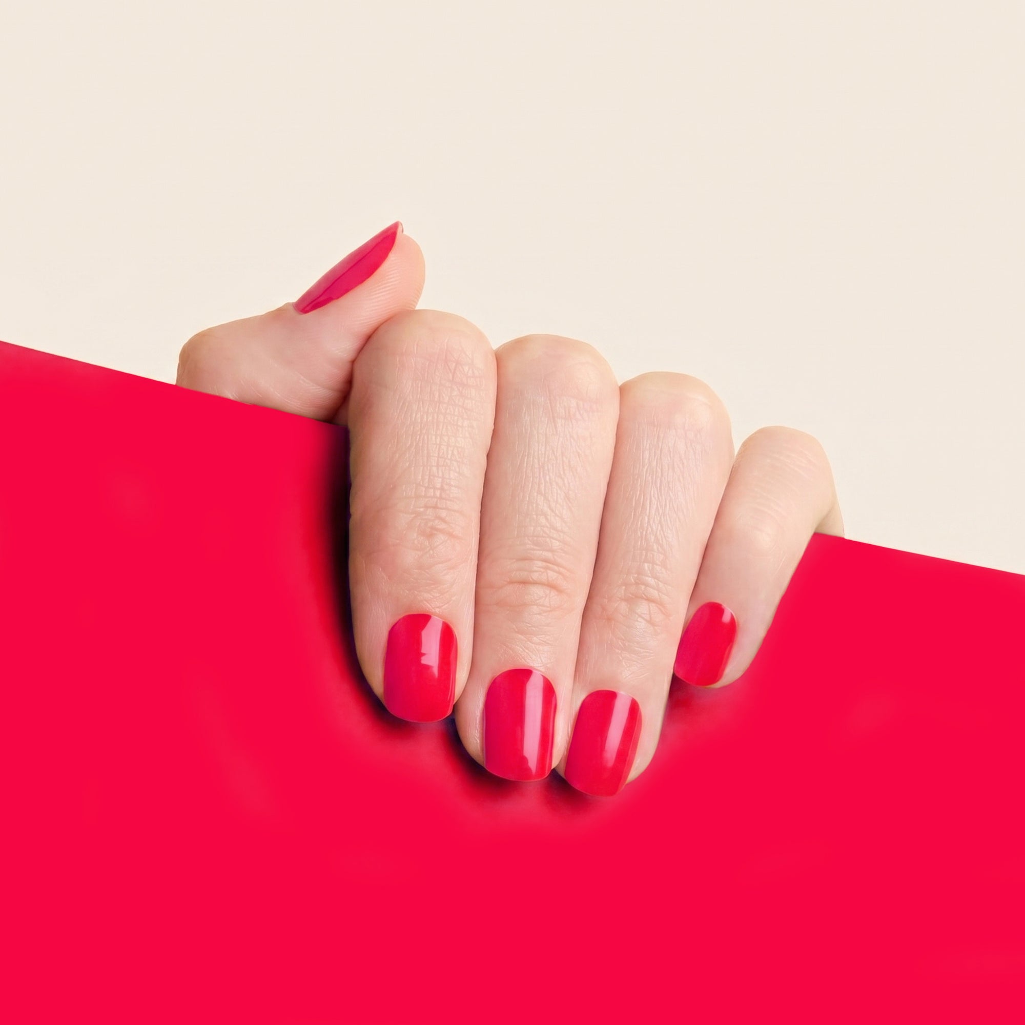 Hand with glossy pink-red Danielle mesme gel nail wraps against a matching bright red background.