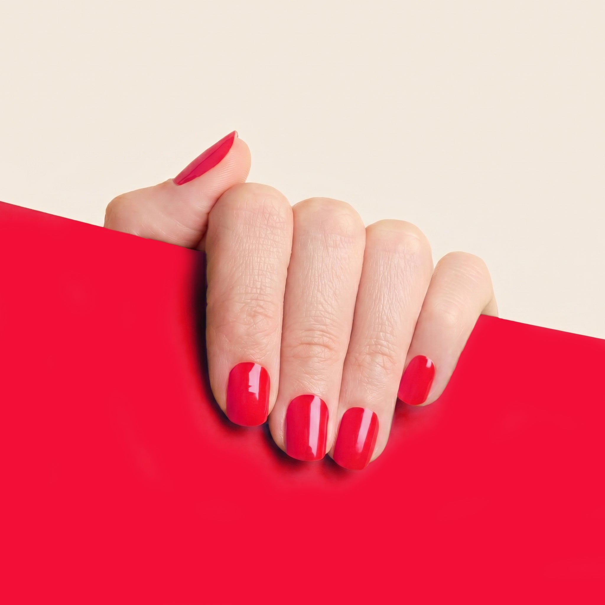 Hand with glossy bright red mesme gel nail wraps against a matching red background.