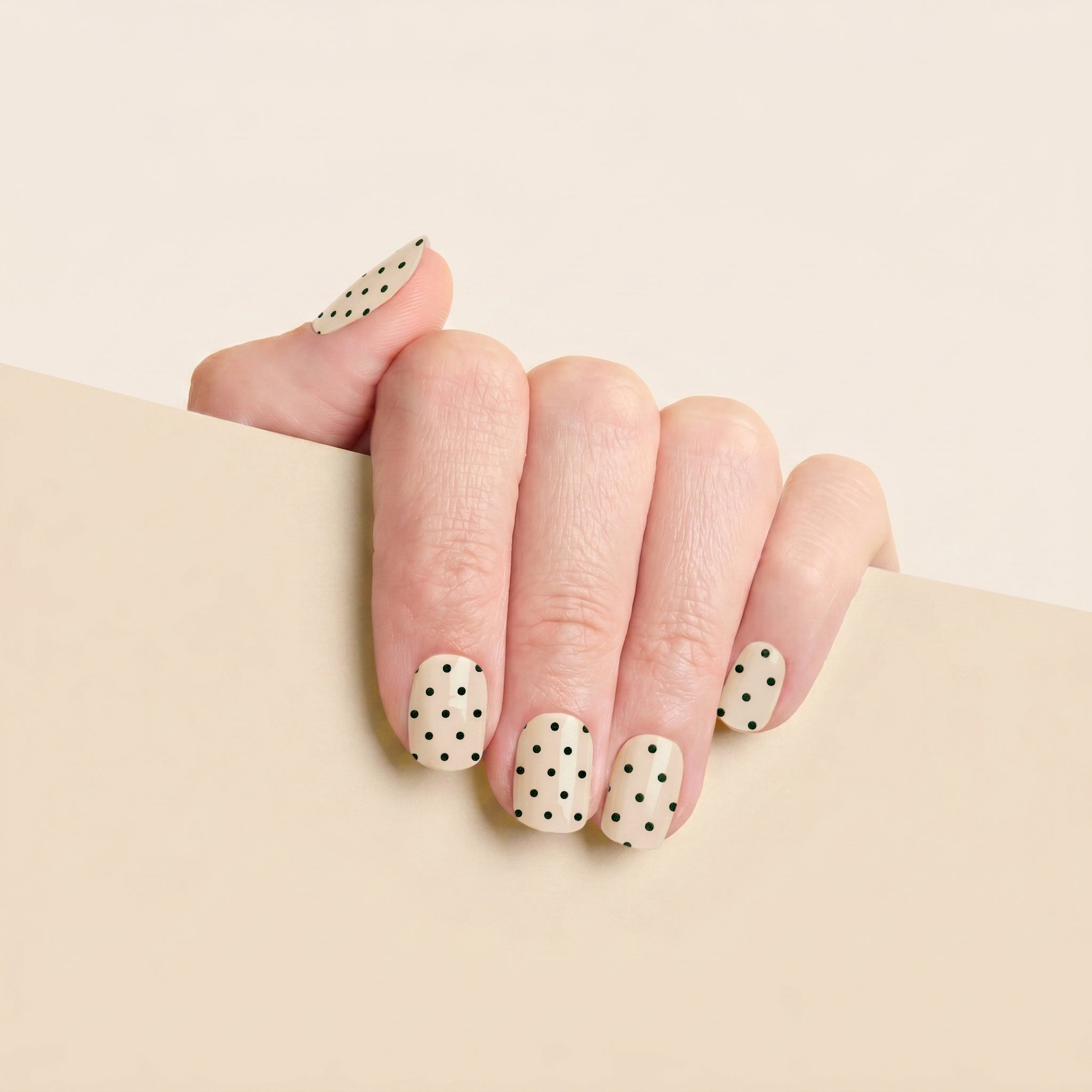 Hand with cream and black polka dot Hannah mesme gel nail wraps against a soft neutral background.