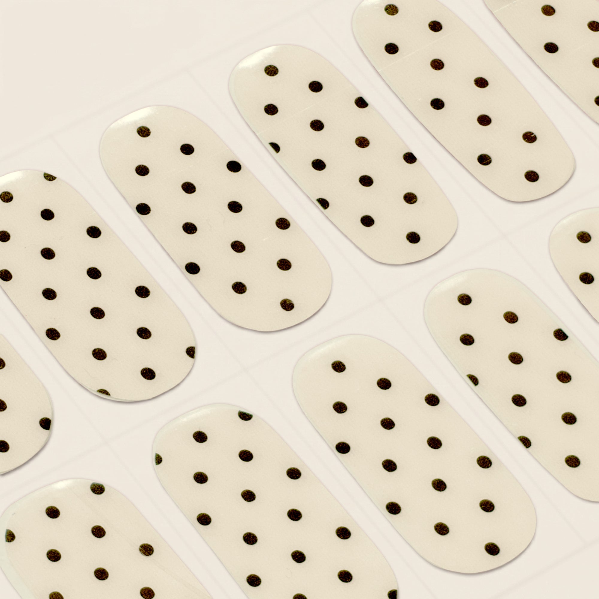 Close-up of Hannah cream and black polka dot mesme gel nail wraps on a sheet.