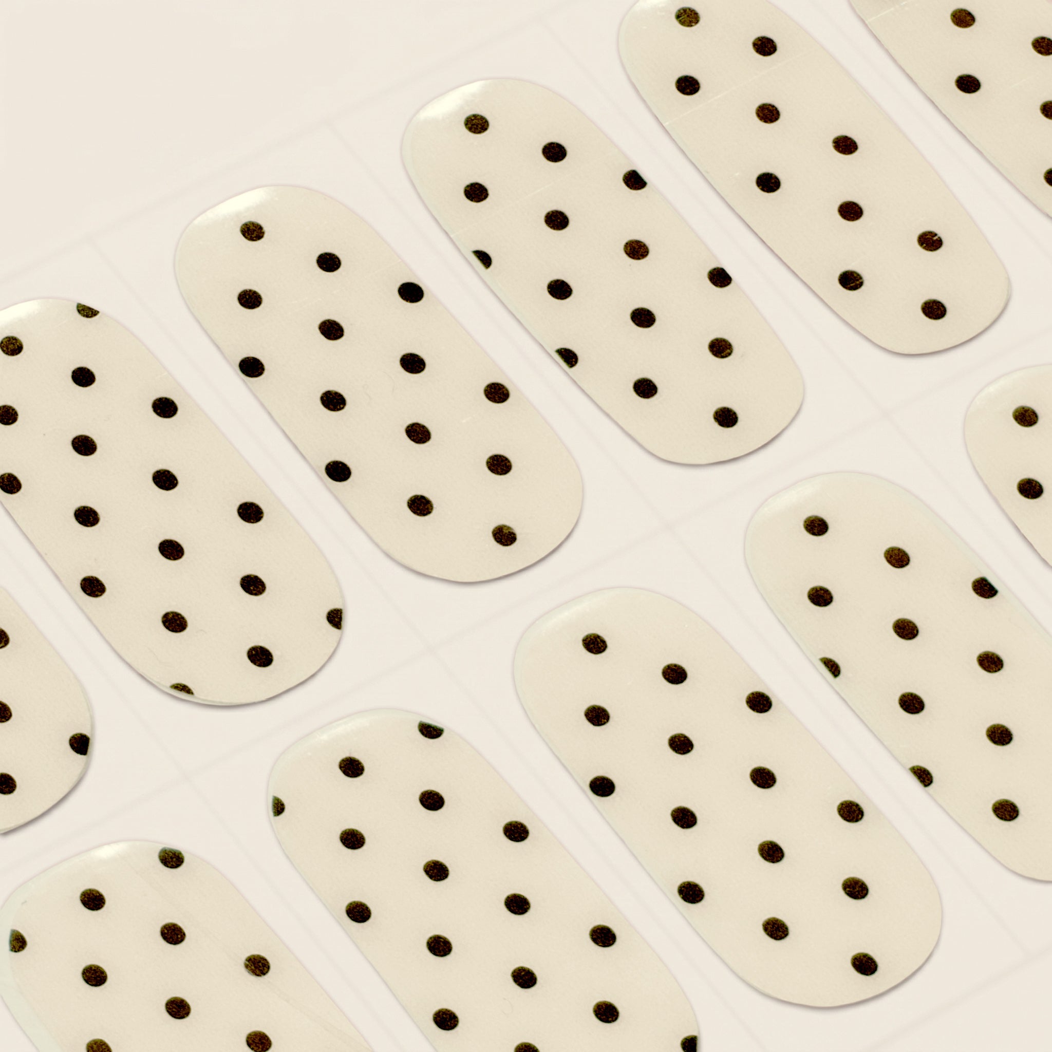 Close-up of Hannah cream and black polka dot mesme gel nail wraps on a sheet.