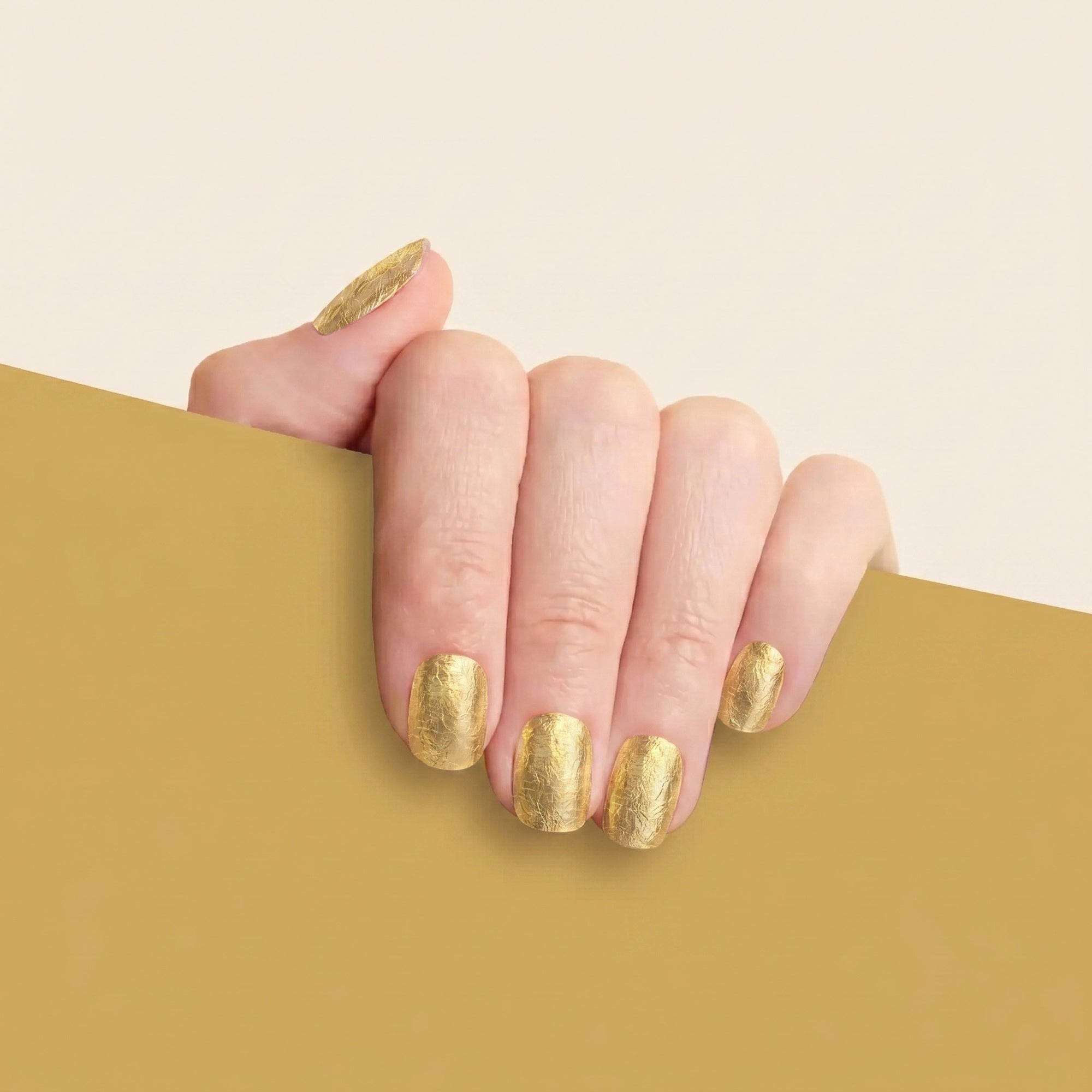 Hand with textured gold metallic mesme gel nail wraps against a gold background.