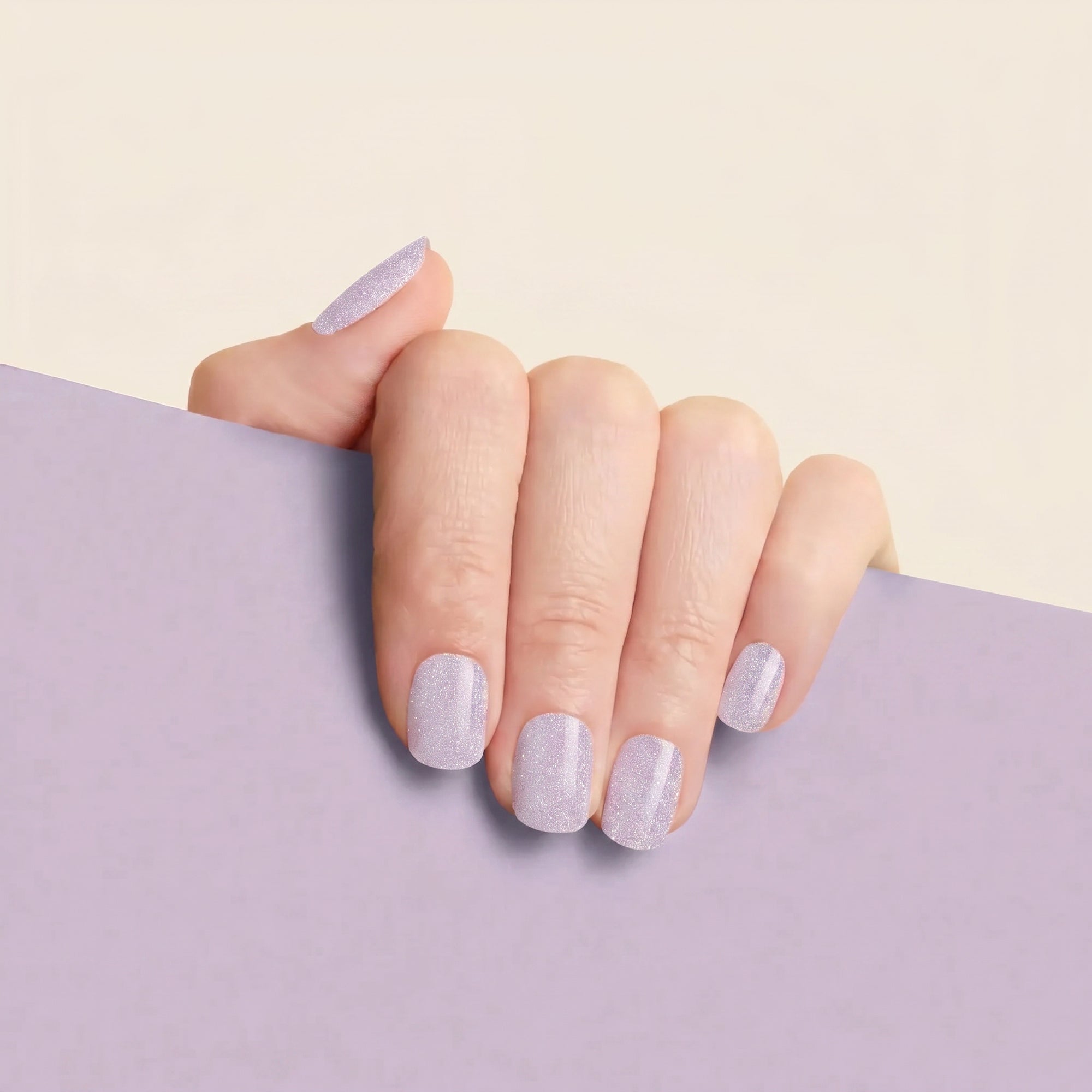 Hand with lilac glitter mesme STAY gel nail wraps against a soft lavender background.