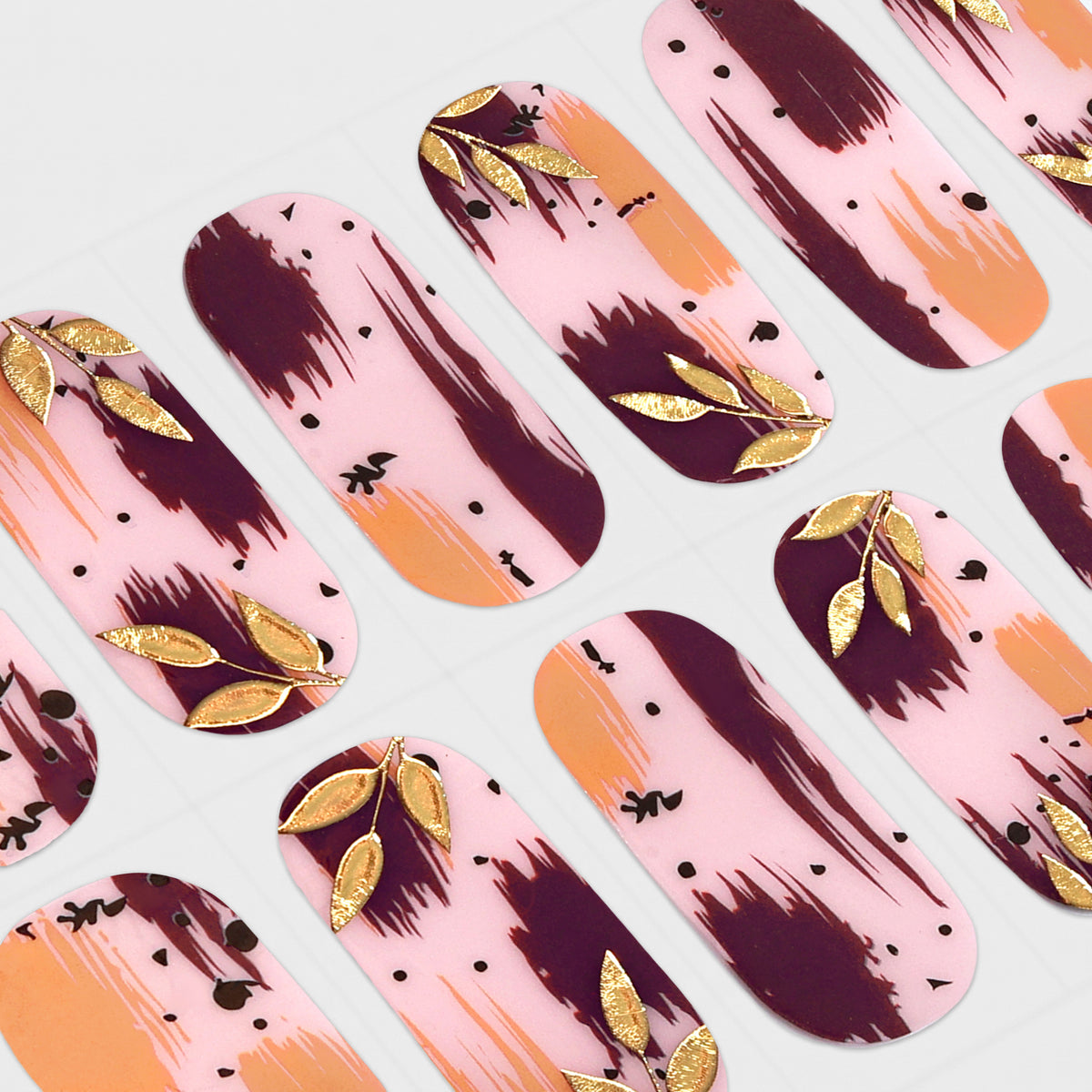 A sheet of mesme nail wraps or stickers with a pink background, dark burgundy brushstroke patterns, orange accents, and metallic gold leaf leaf designs, arranged diagonally on a white grid backing.