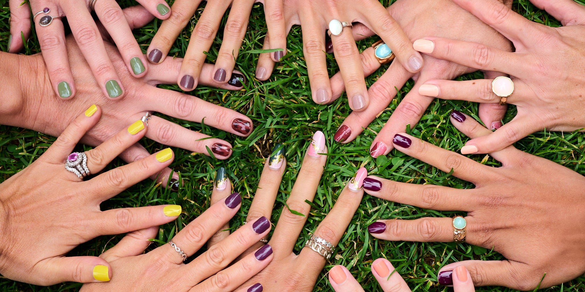 Multiple hands with painted nails and rings on a grass background