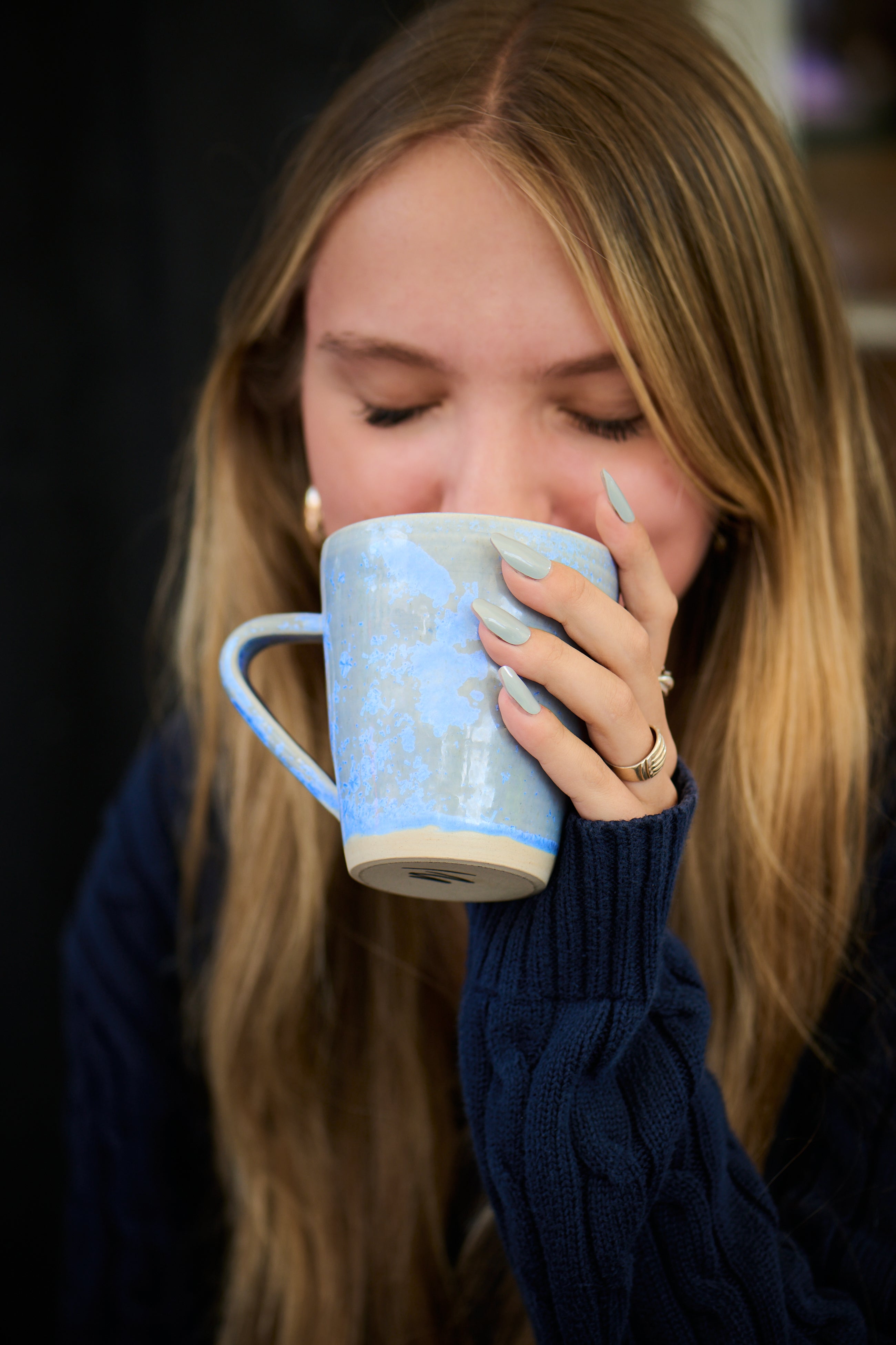 Woman drinking from a blue mug with a patterned design wearing blue mesme nail wraps