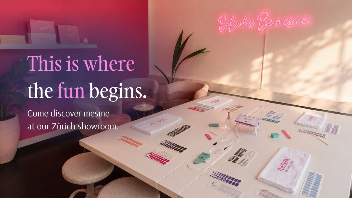 A styled interior mesme showroom scene showing a white table covered with nail wrap samples, swatches, and branded items, with chairs and a plant in a warm room. Large overlaid text reads 'This is where the fun begins.