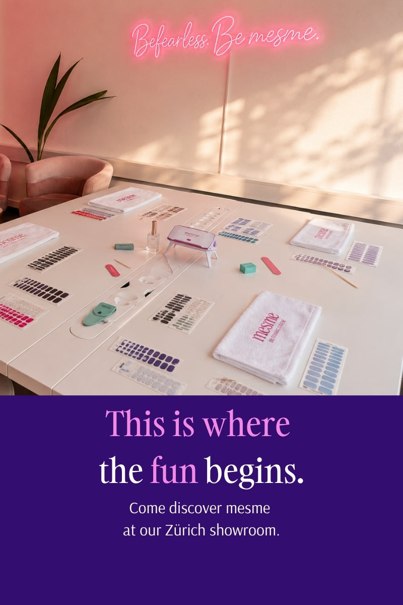 A promotional interior scene showing a table covered with nail color samples, swatches, and a branded white towel in a softly lit room. A pink neon-style sign at the top reads 'Be fearless, Be mesme.